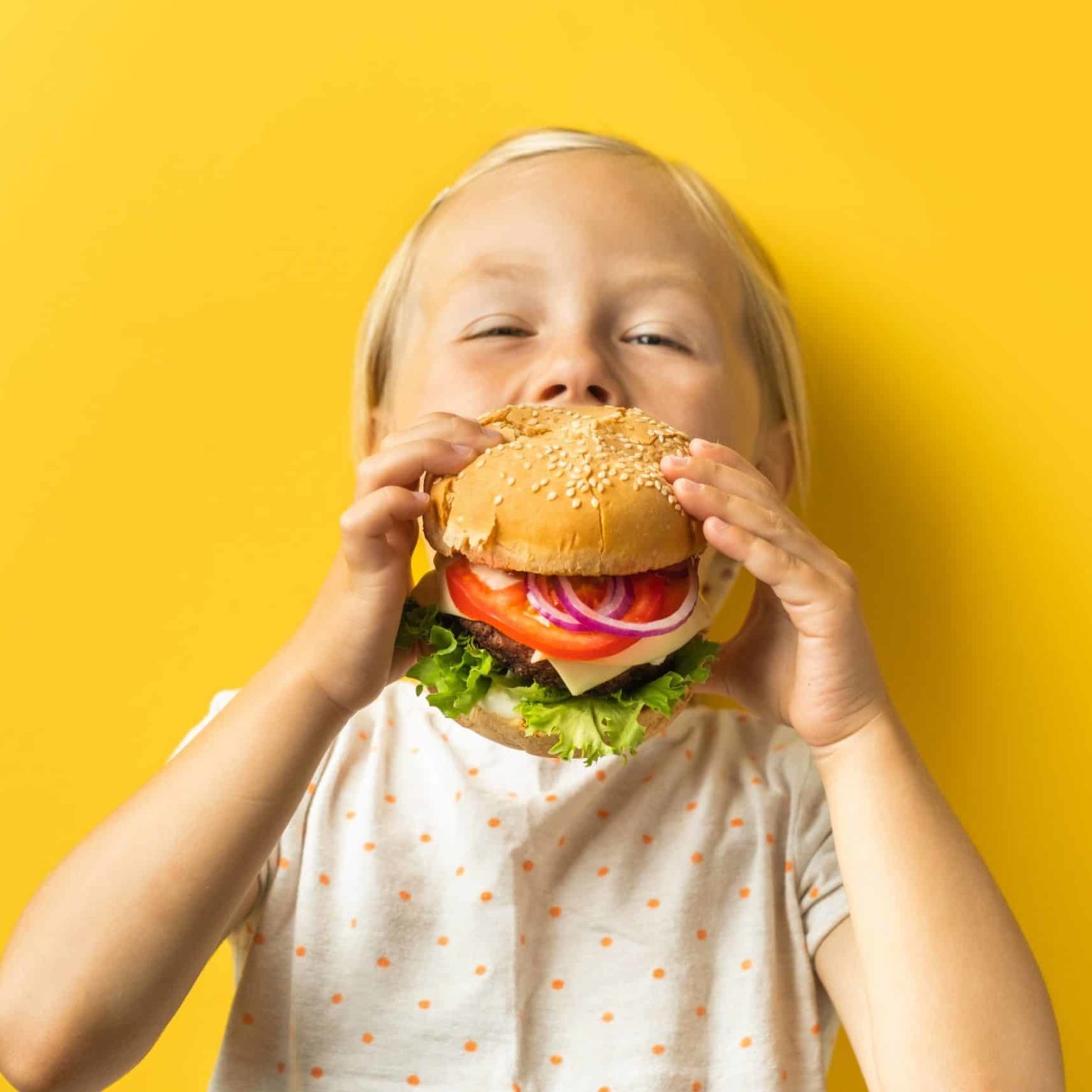 Happy blonde haired caucasian young girl eating a burger