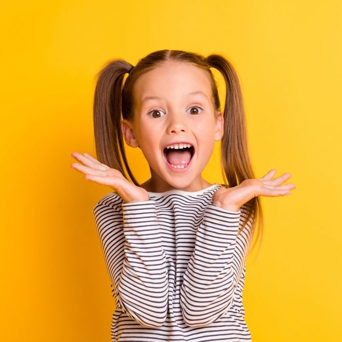 excited young girl with pigtails on yellow background